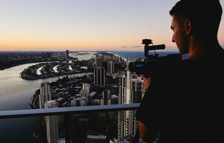 A young man holding a video camera and looking at the city shore