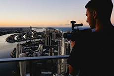 A young man holding a video camera and looking at the city shore