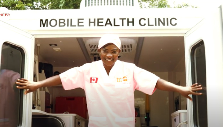 A smiling midwife holds open the doors at the back of a vehicle.