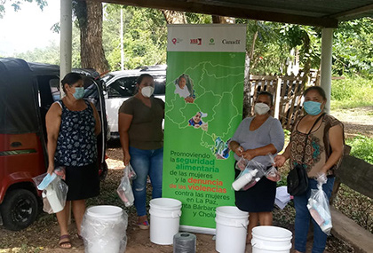 Four women wearing protective masks stand by a poster. The text of the poster is in Spanish, and the Canada wordmark is visible.