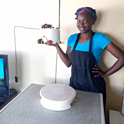 A woman smiles as she holds up a fancy cake on a plate.