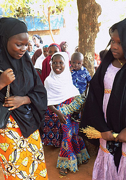 A dozen people are gathered around a water hand-pump