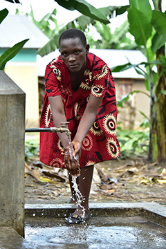 Shildah Nabimanya washing her hands, using a tap outside.