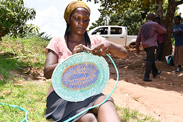 Shildah Nabimanya sitting, weaving a colourful basket.