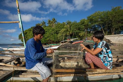 A man and a woman sitting on a boat hold a fishing net between them.