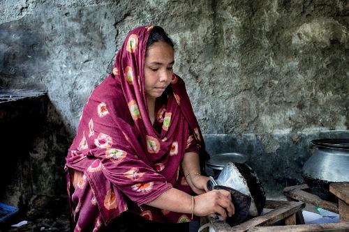 A woman in a purple, patterned hijab drains a pot.