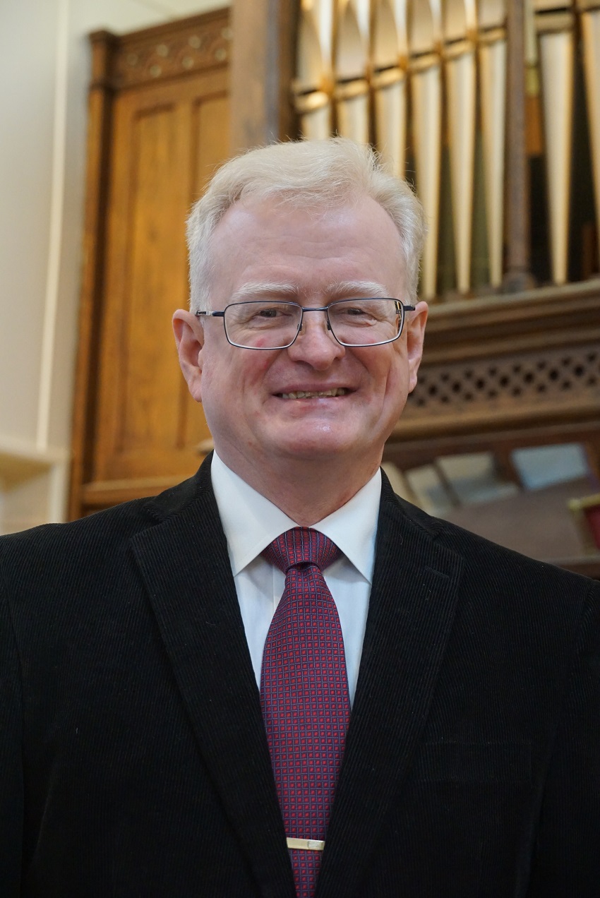 A man wearing a suit and glasses smiles.