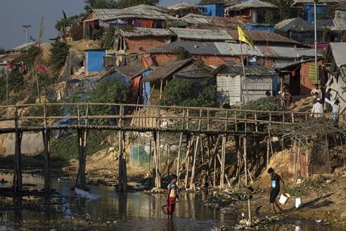 Deux enfants marchant vers une rivière; un pont et un camp de réfugiés sont en arrière-plan.