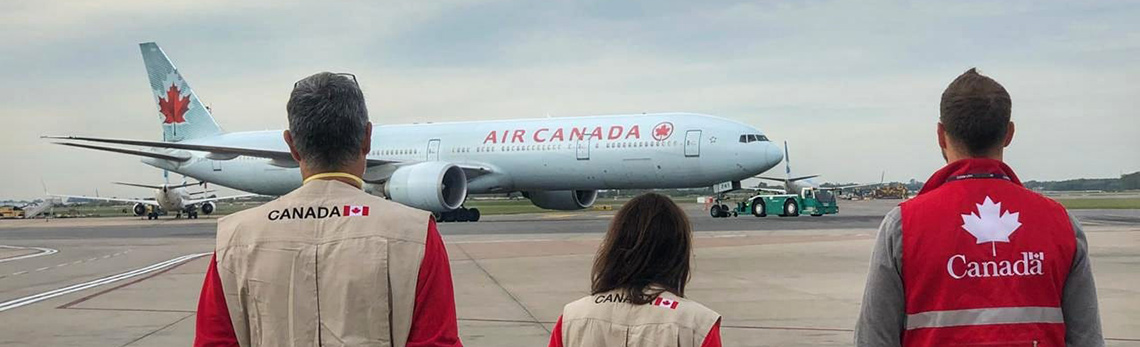 Trois agents canadiens sur le tarmac, observant un avion passager.