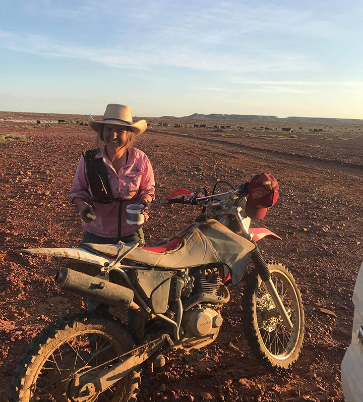 Femme dans un champ de terre, debout derrière une moto tout-terrain