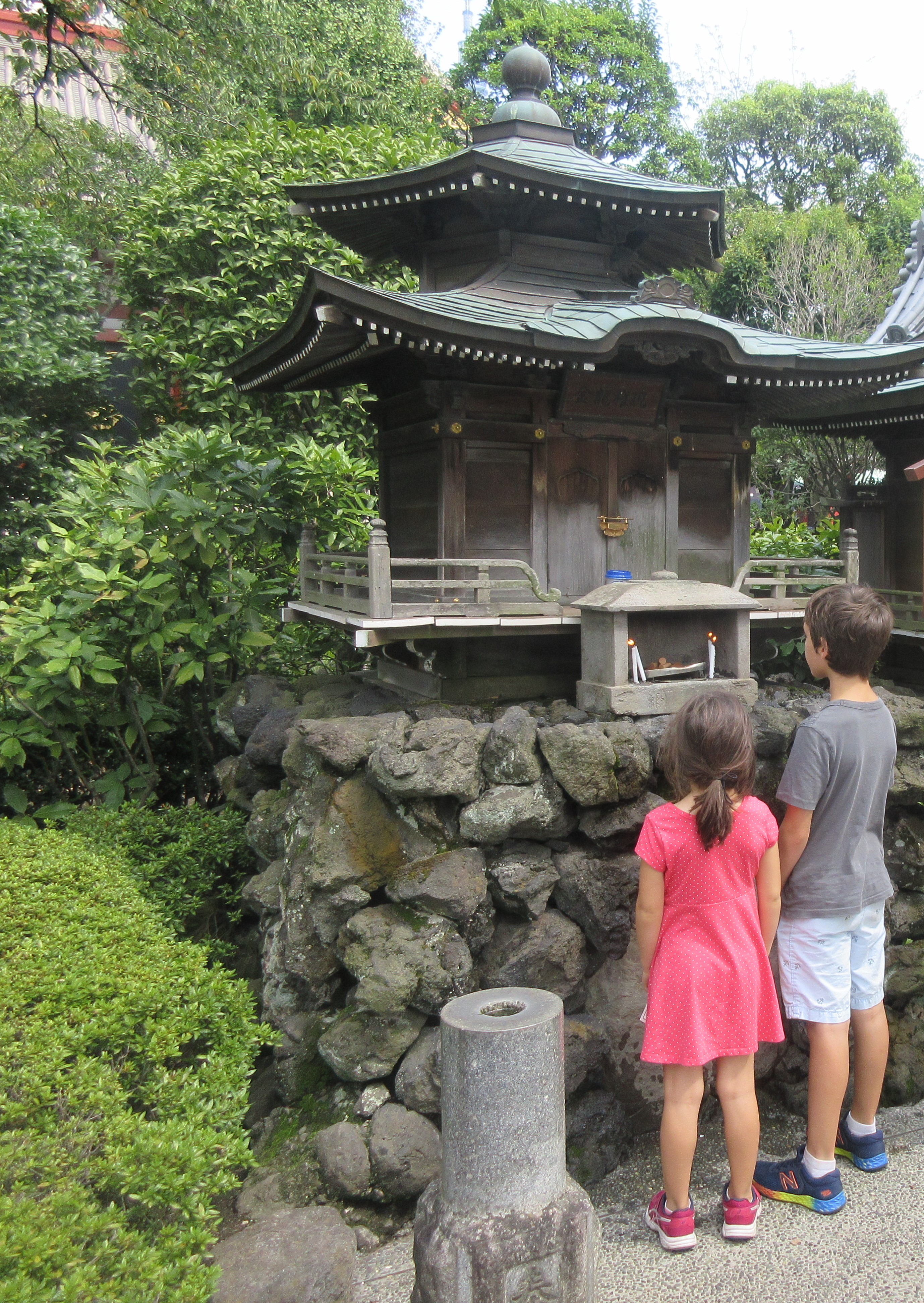 Two kids in front of a small religious monument.