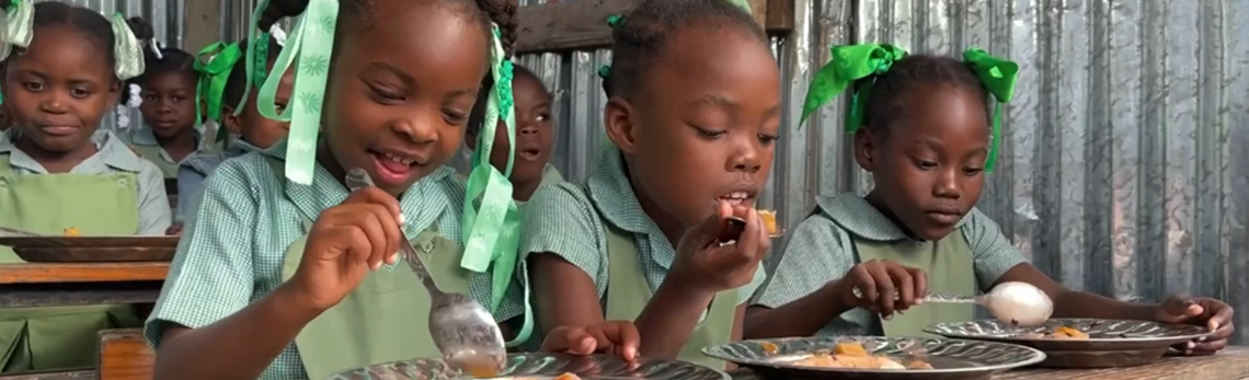 Des petites filles mangent un repas offert à l’école grâce au projet Cantines scolaires et achats locaux. (Source : Programme alimentaire mondial)