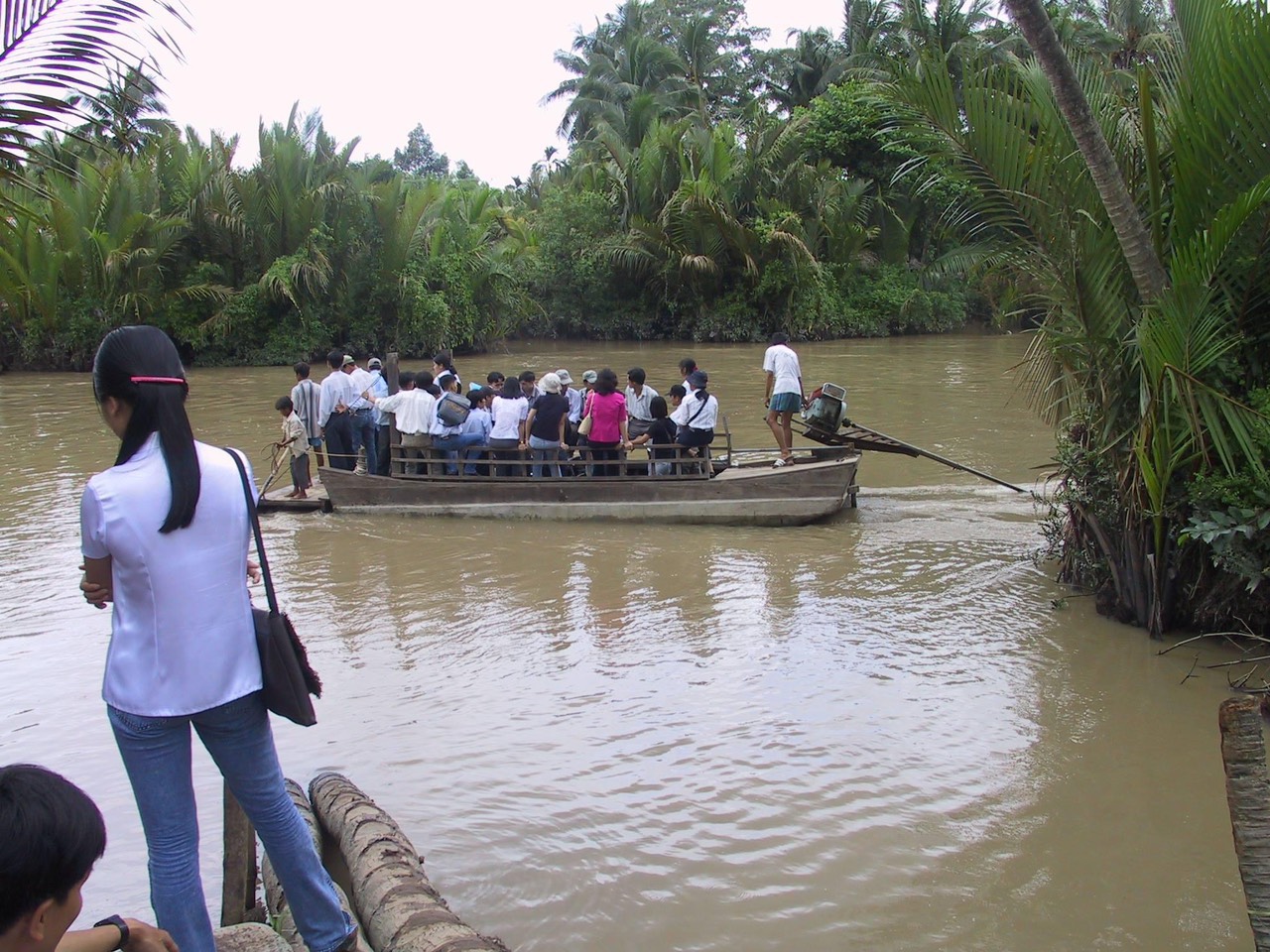 Students and staff crossing a muddy river on a long low motorboat to get to school.
