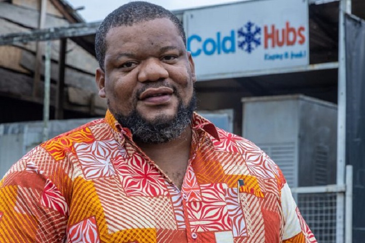 Figure 8: A man wearing an orange shirt in front of a building with a sign that reads: “Cold Hubs.”