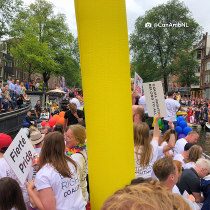 Canadian embassy staff celebrating Pride season in the Netherlands. Staff are waving to the crowd in their decorated boat that is part of the annual Canal Parade in Amsterdam.