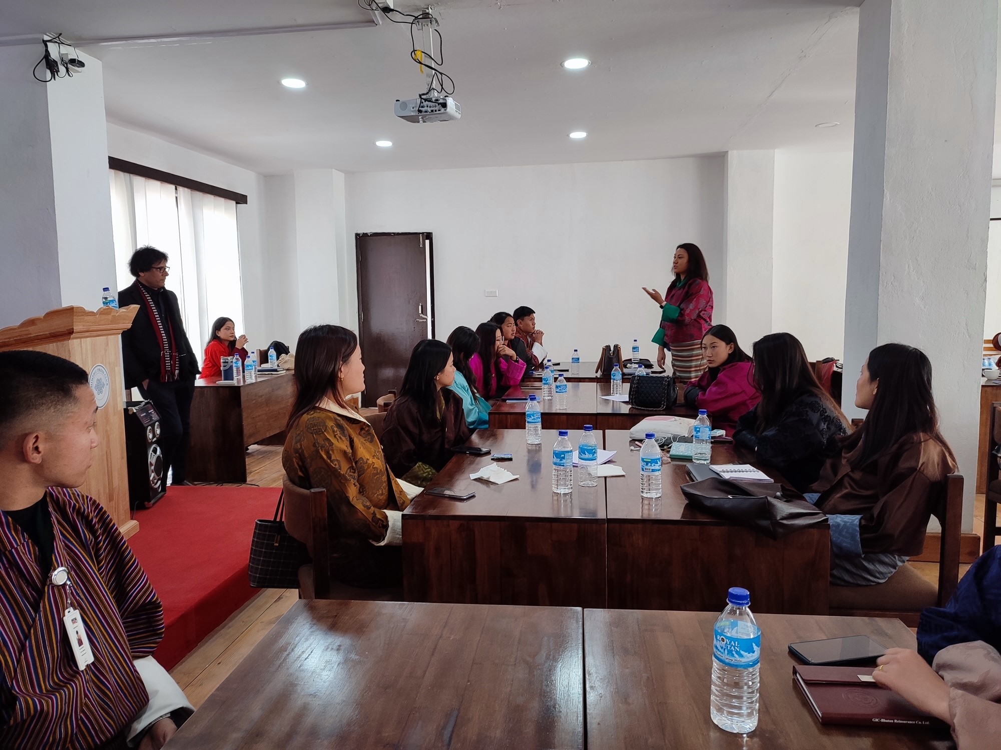 A woman stands at a table and people who are seated listen to her speak.