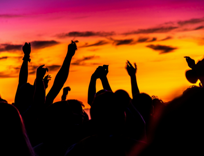 Un groupe de personnes danse au coucher du soleil. Le ciel passe du rose à l'orange.